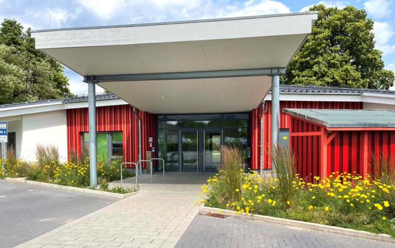 Das Gebäude der Kindertagesstätte "Unter dem Lüningsberg" im Kirchenkreis Hameln-Pyrmont, ein modernes, rotes Gebäude mit großen Fenstern und einem imposanten Eingangsbereich.