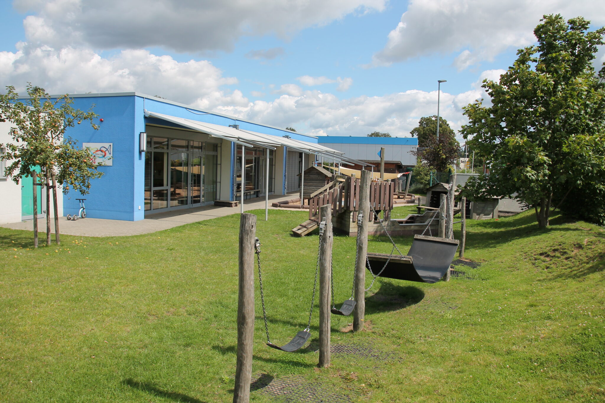 Die Kindertagesstätte "Kleiner Eugen", ein gemütliches Gebäude mit einem grünen Garten und einem Spielplatz im Vordergrund.